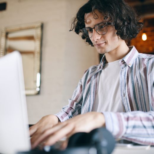 Serious male economist making financial report, counting amount of sales using information from corporative database. Young skilled computer programmer in eyewear typing on laptop, testing code Serious male economist making financial report, counting amount of sales using information from corporative database. Young skilled computer programmer in eyewear typing on laptop, testing code